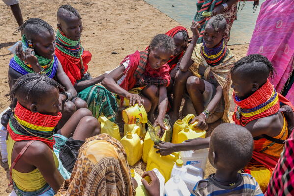Turkana women and children filling multiple yellow jerrycans at a shallow water source