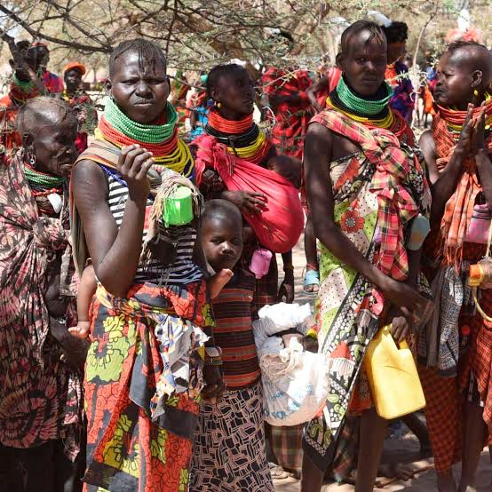 Turkana community in colourful traditional dress holding water jerrycans in arid landscape